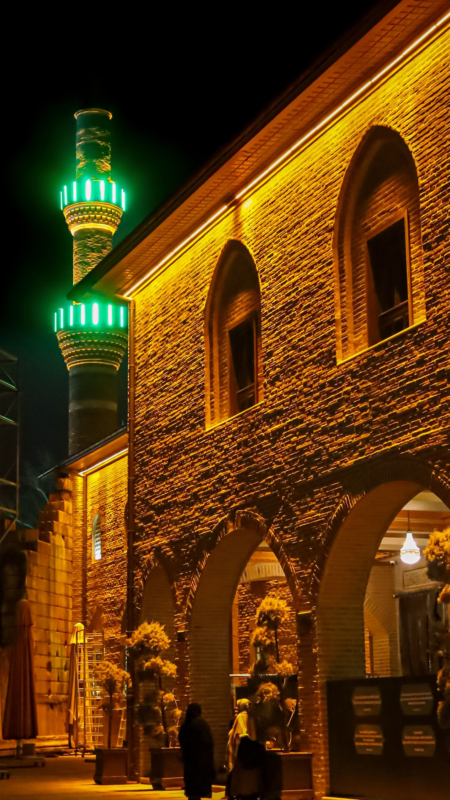 A beautifully lit mosque facade with green-lit minaret during the night.