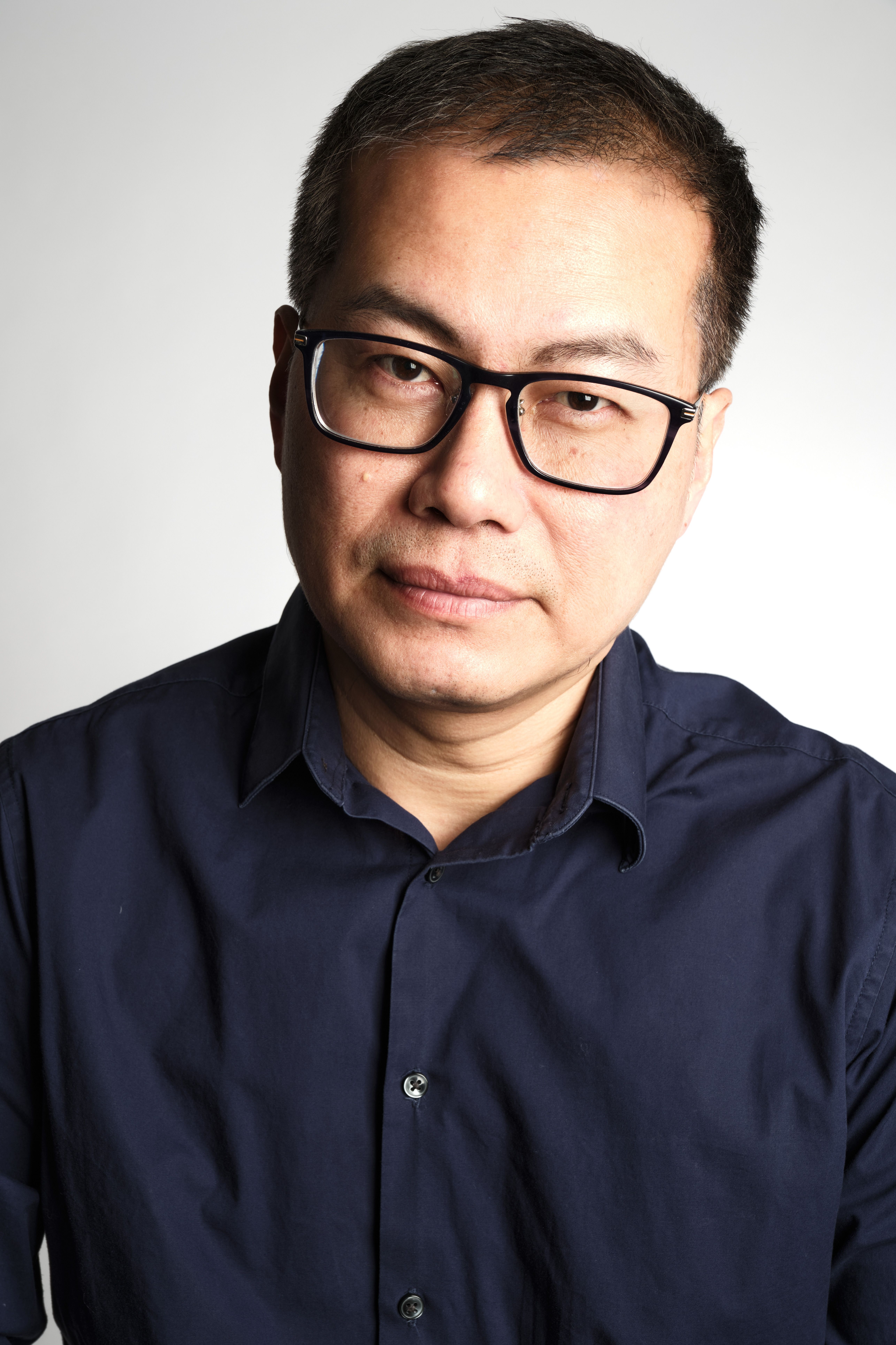 Portrait of an adult man wearing glasses and a navy shirt, looking confidently at the camera.
