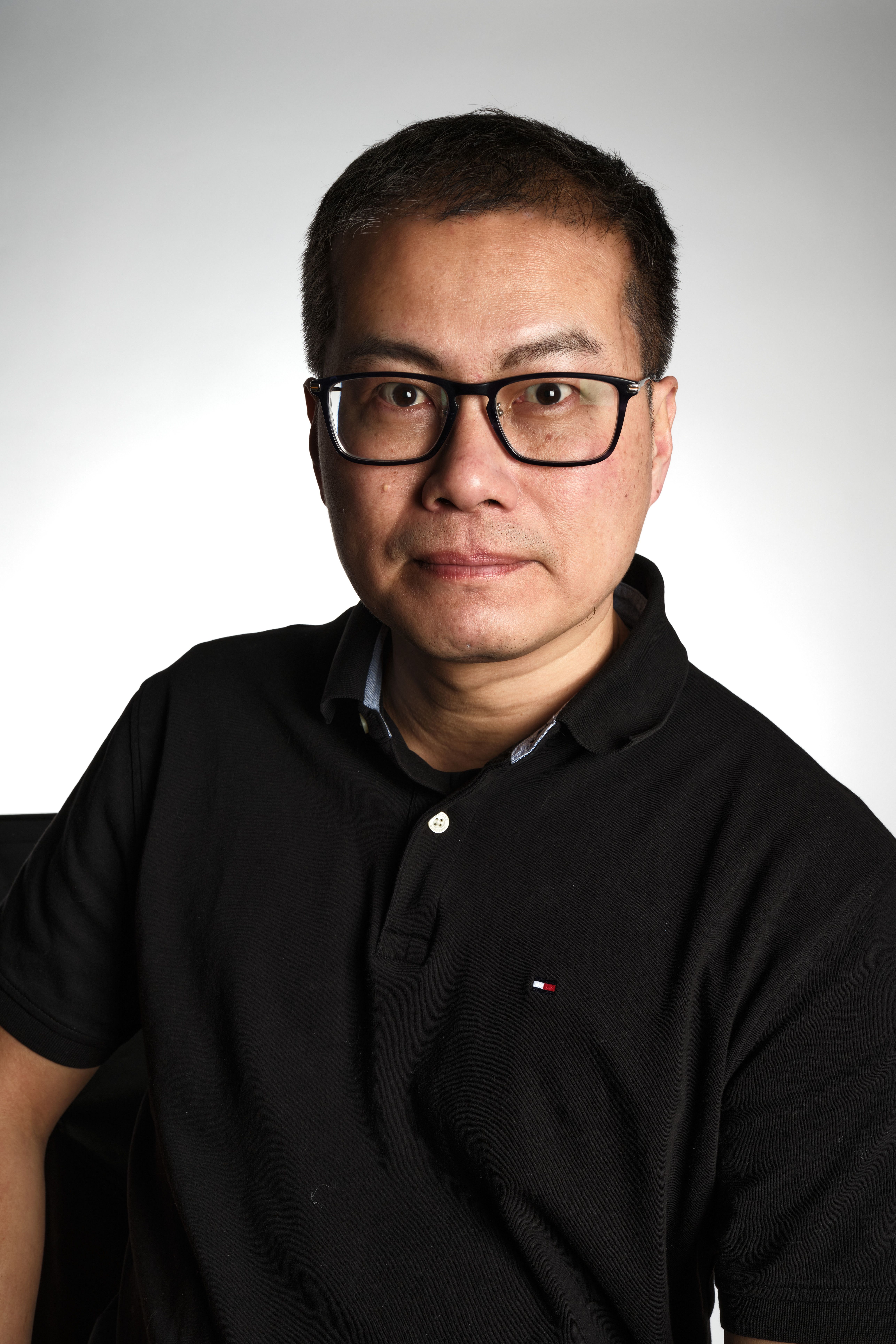 Studio portrait of an adult man wearing glasses and a black shirt against a neutral background.