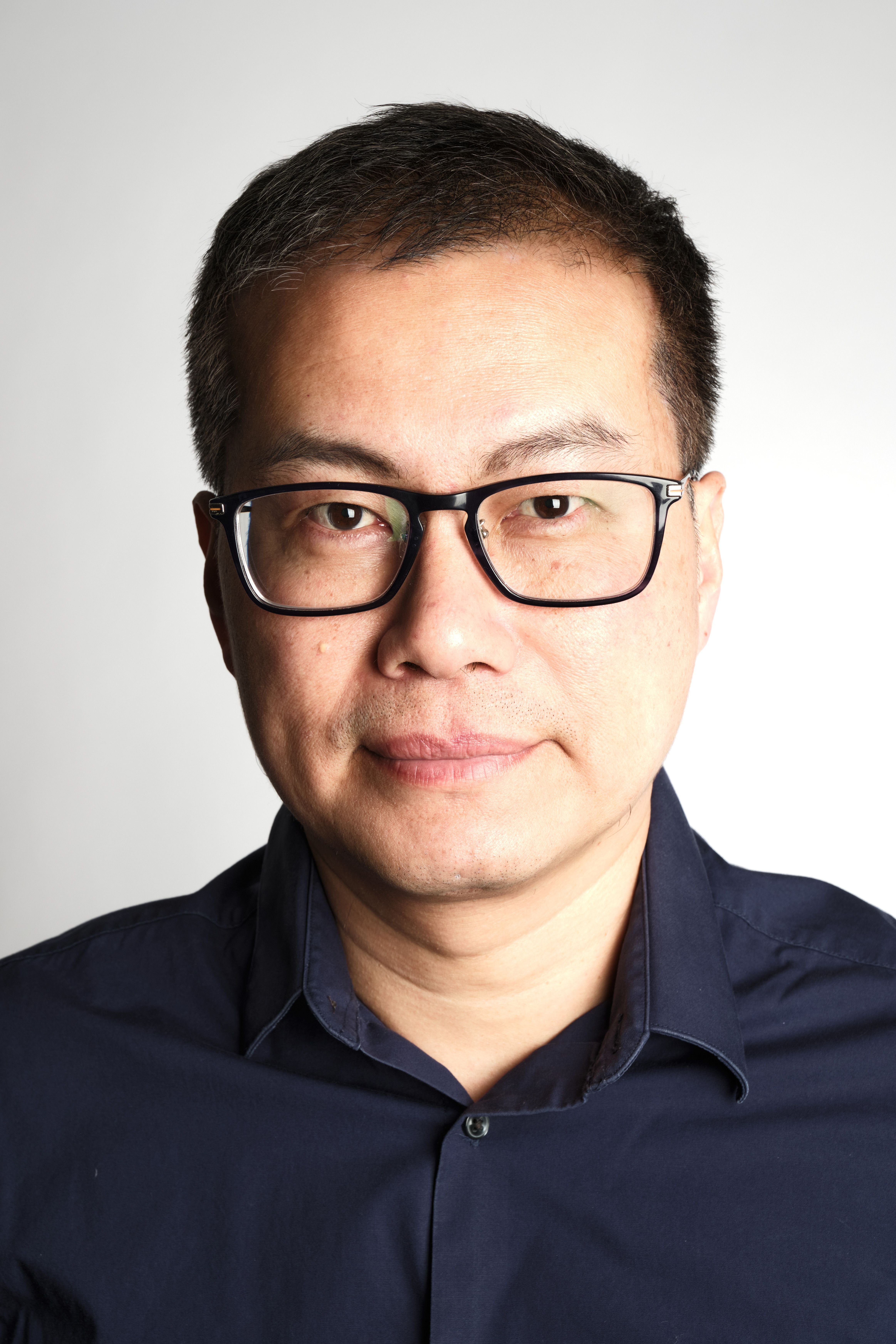 Close-up portrait of an adult man wearing glasses against a neutral background.