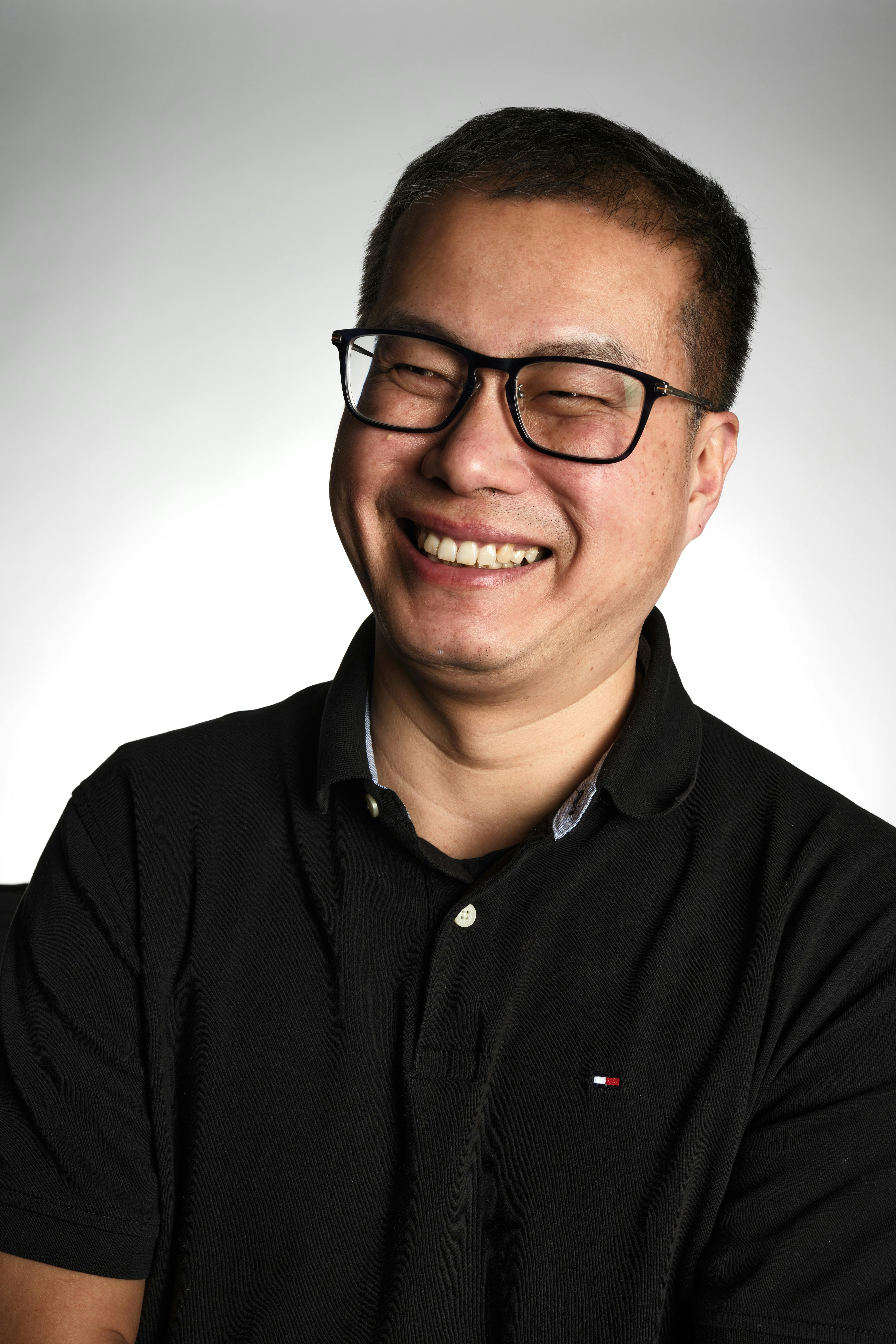 Portrait of a happy man wearing glasses and a black polo shirt, smiling warmly.