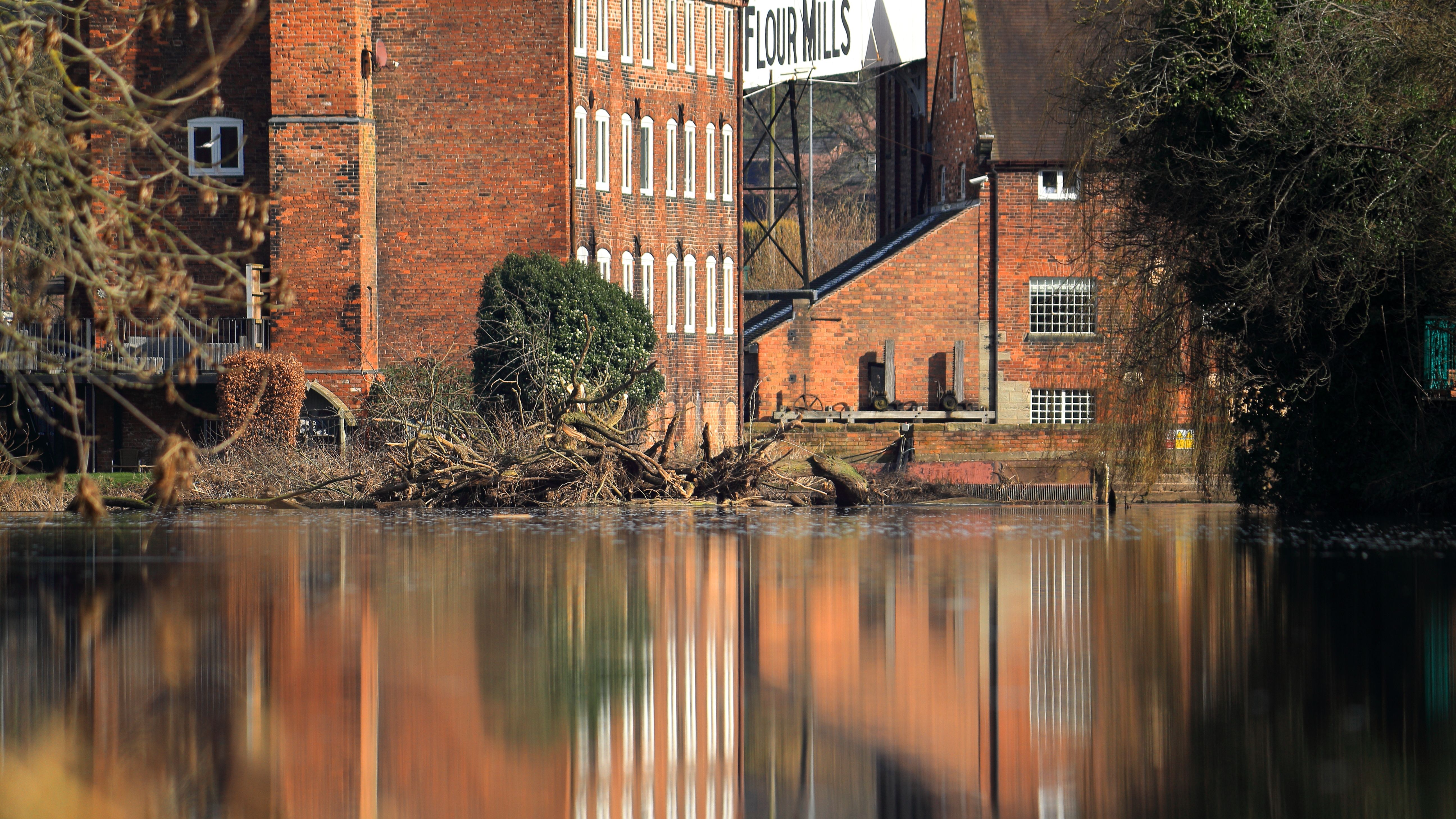 A tranquil scene of a historic flour mill reflected in calm river waters.