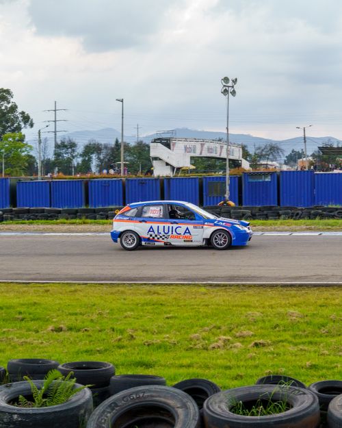 Free Blue racing car speeding on an outdoor track, surrounded by lush landscape and cloudy sky. Stock Photo