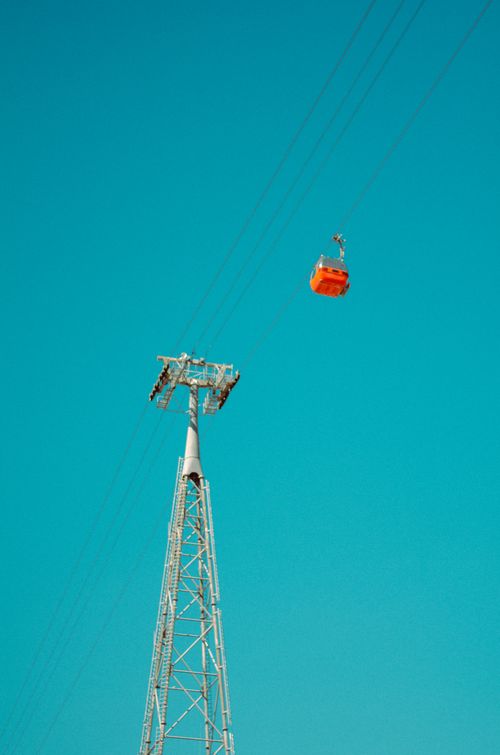 Free Vibrant orange cable car suspended on wires against a clear blue sky, minimalistic composition. Stock Photo