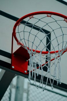 Detailed shot of a basketball hoop with a red rim and net in an outdoor sports court.