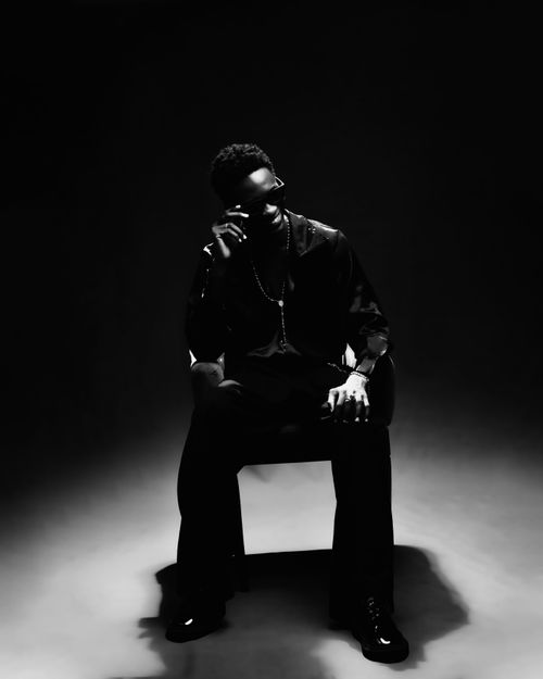 Free Dramatic black and white portrait of a man in fashion-forward attire sitting confidently in shadows. Stock Photo