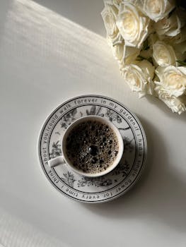 Elegant coffee cup on floral saucer with white roses creating a cozy vibe.