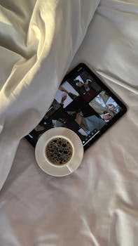 A cozy setup with a coffee cup next to a tablet on a bed.