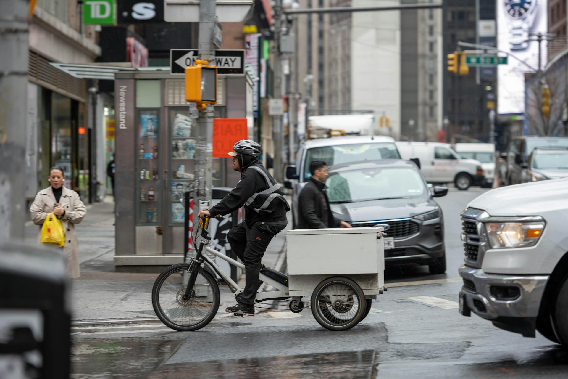 Cyclist on delivery bike amidst busy New York City street with pedestrians and vehicles.