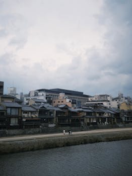 Traditional Japanese houses along the Kamo River in Kyoto under a cloudy sky.
