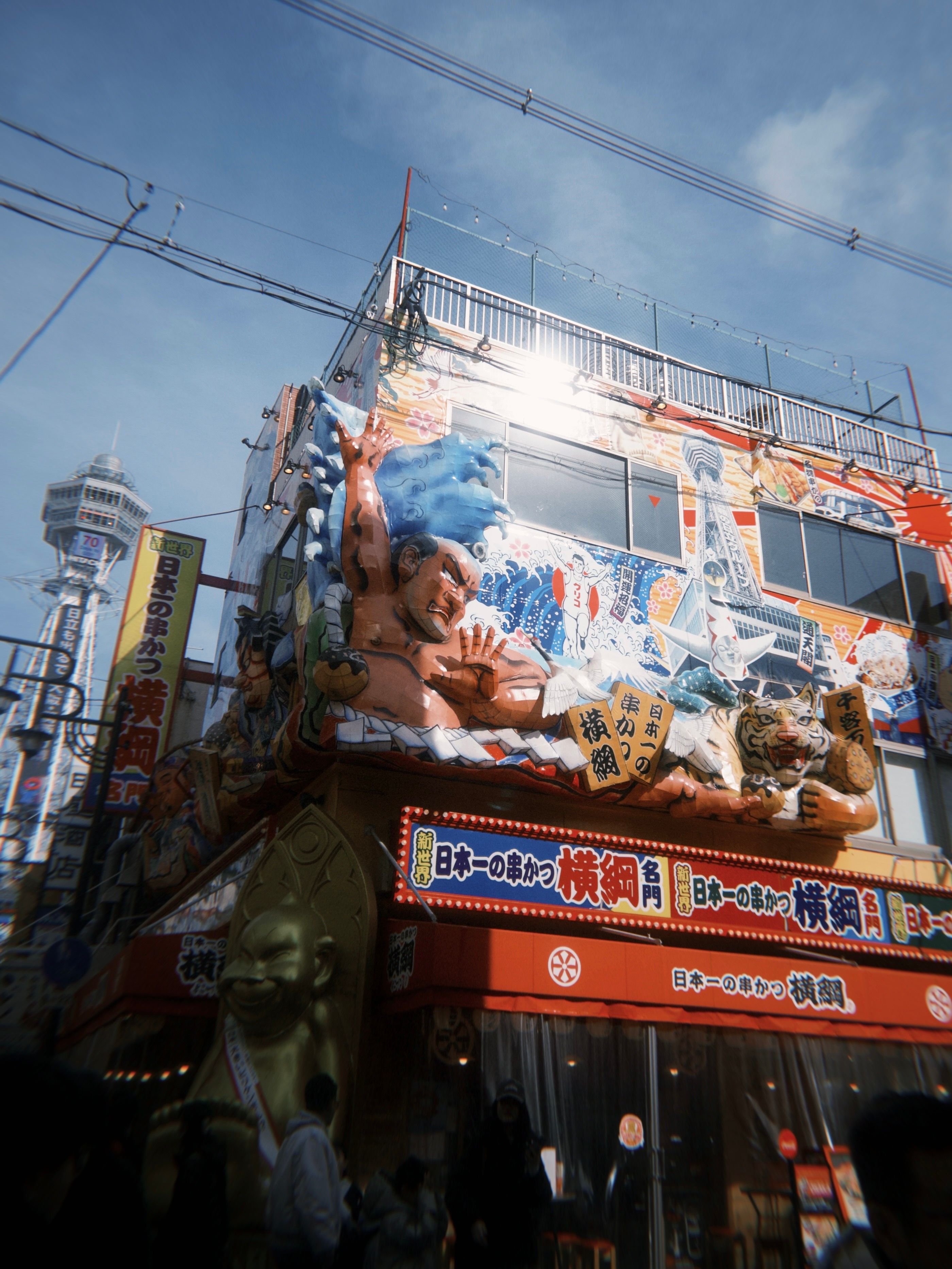Vibrant shopfront in Osaka featuring traditional Japanese art and Tsūtenkaku Tower.