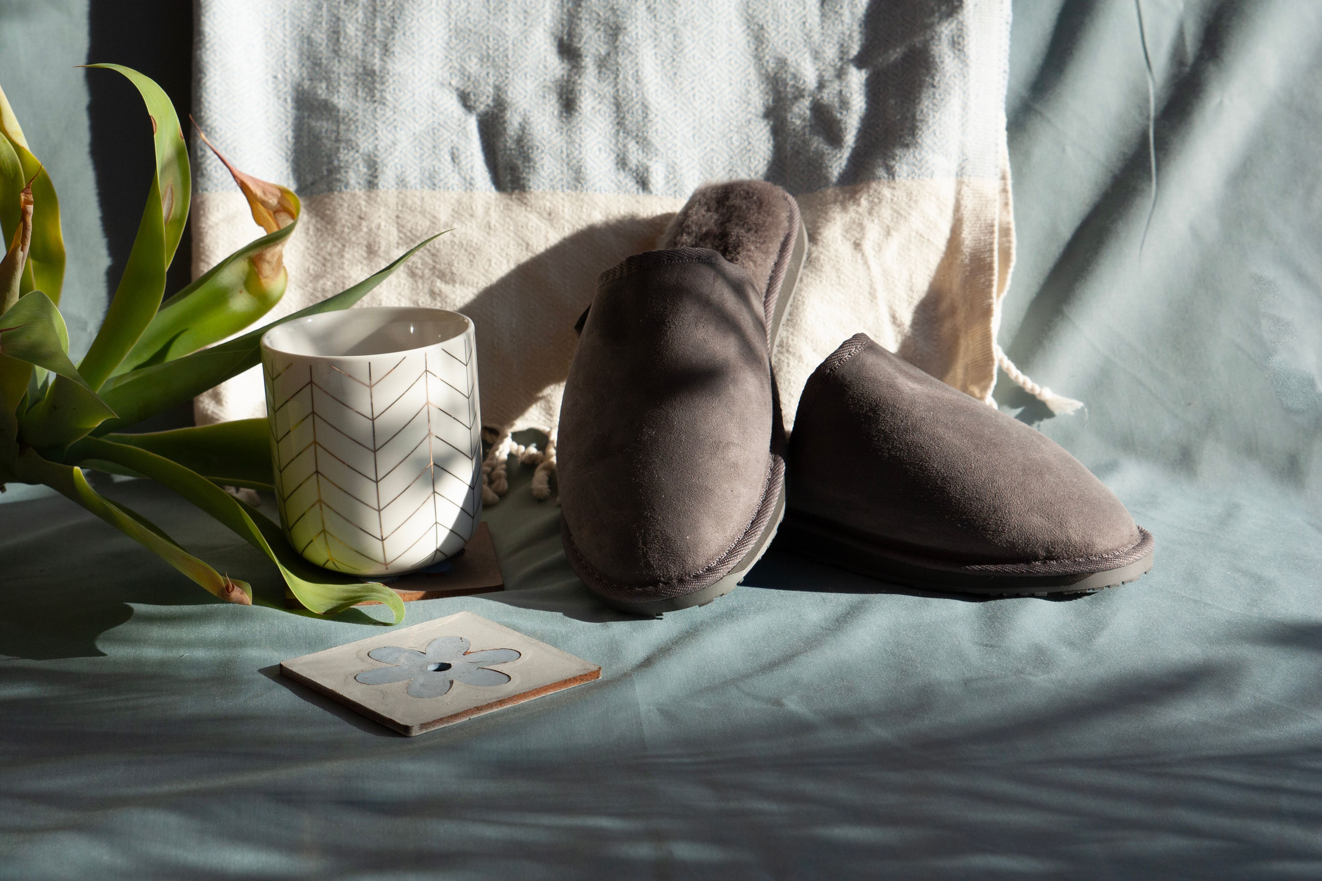 Grey suede mule slippers on a pale blue throw beside a white mug