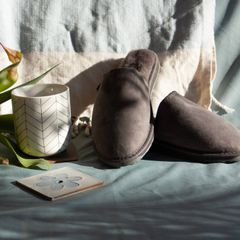 Grey suede mule slippers on a pale blue throw beside a white mug