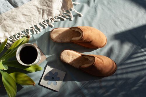 Free Warm morning scene with slippers, coffee, and natural light on a soft surface. Stock Photo