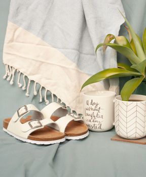 Chic arrangement of sandals, decorative mugs, and a plant creating a cozy vibe. Perfect for lifestyle themes.