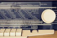 A detailed view of a vintage radio's tuning dial with city stations displayed.