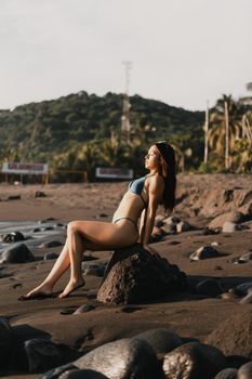 A Latina woman in a bikini enjoys the sun on a rocky tropical beach during summer.