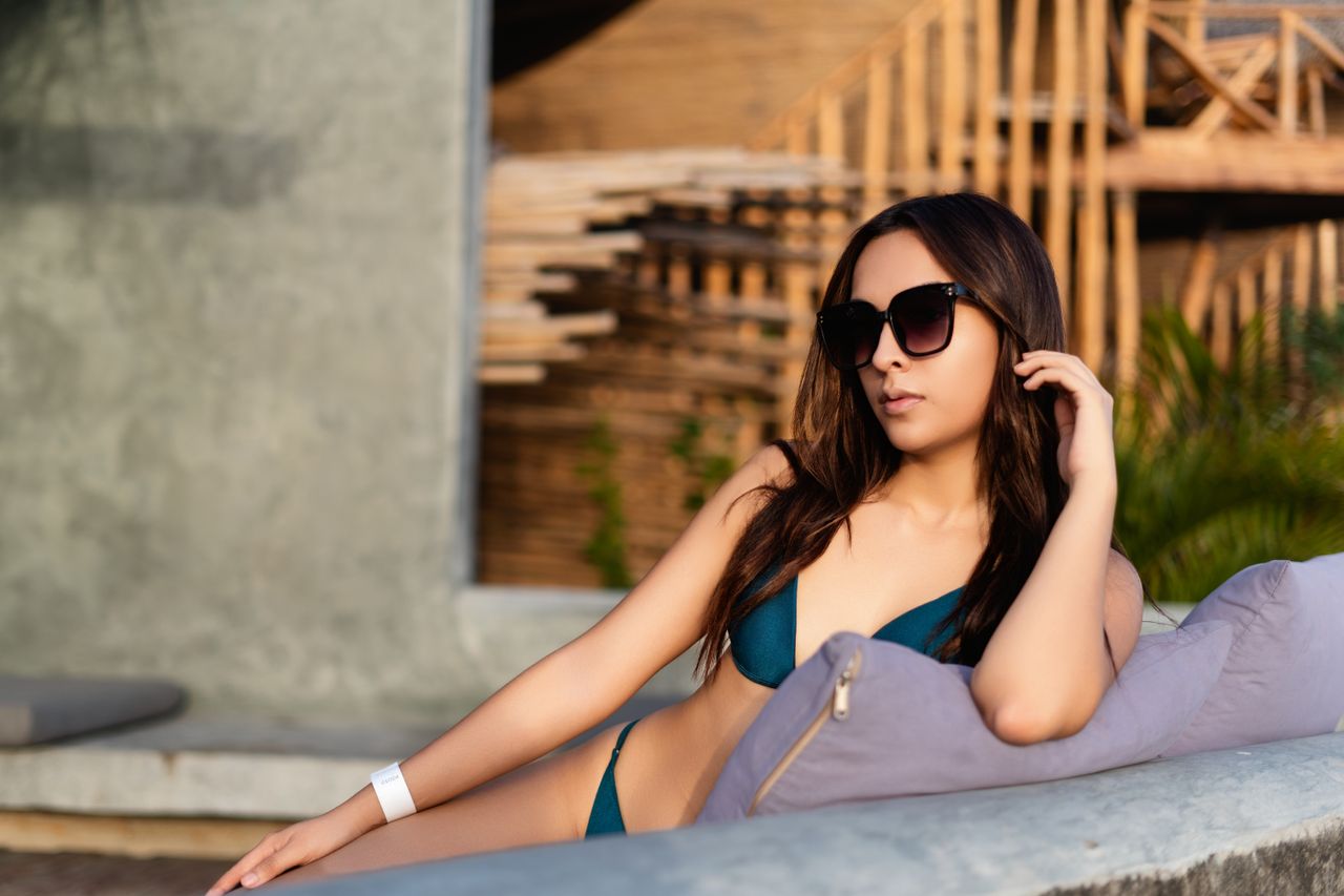 model in sunglasses lounging by the beachside in a bikini enjoying a s