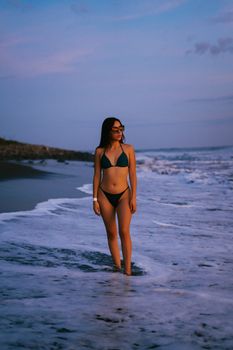Woman in a bikini enjoying a tranquil beach walk during sunset, capturing summer vibes.