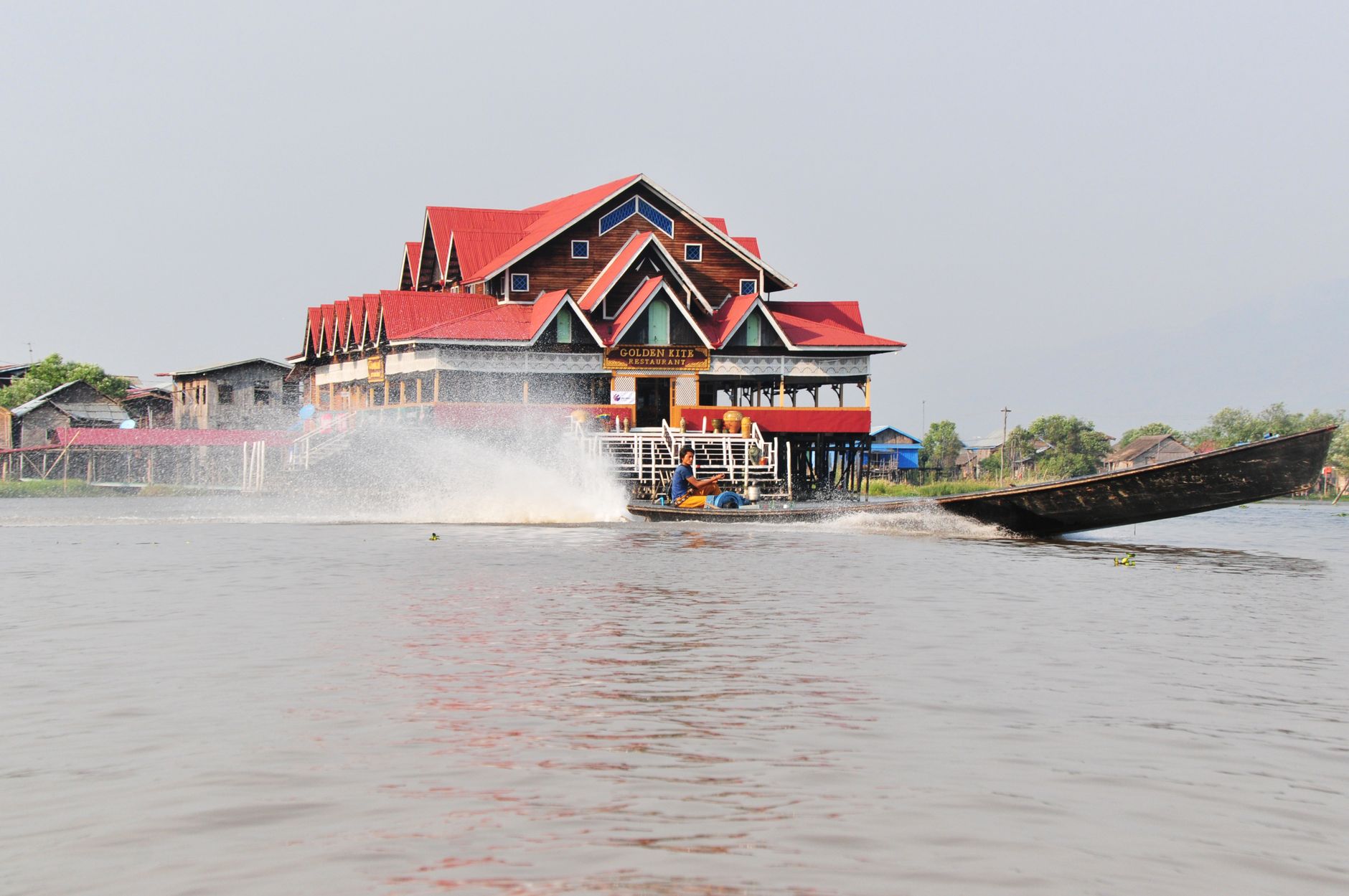 A vibrant boat speeds by a traditional wooden structure on Inle Lake, Shan, Myanmar.
