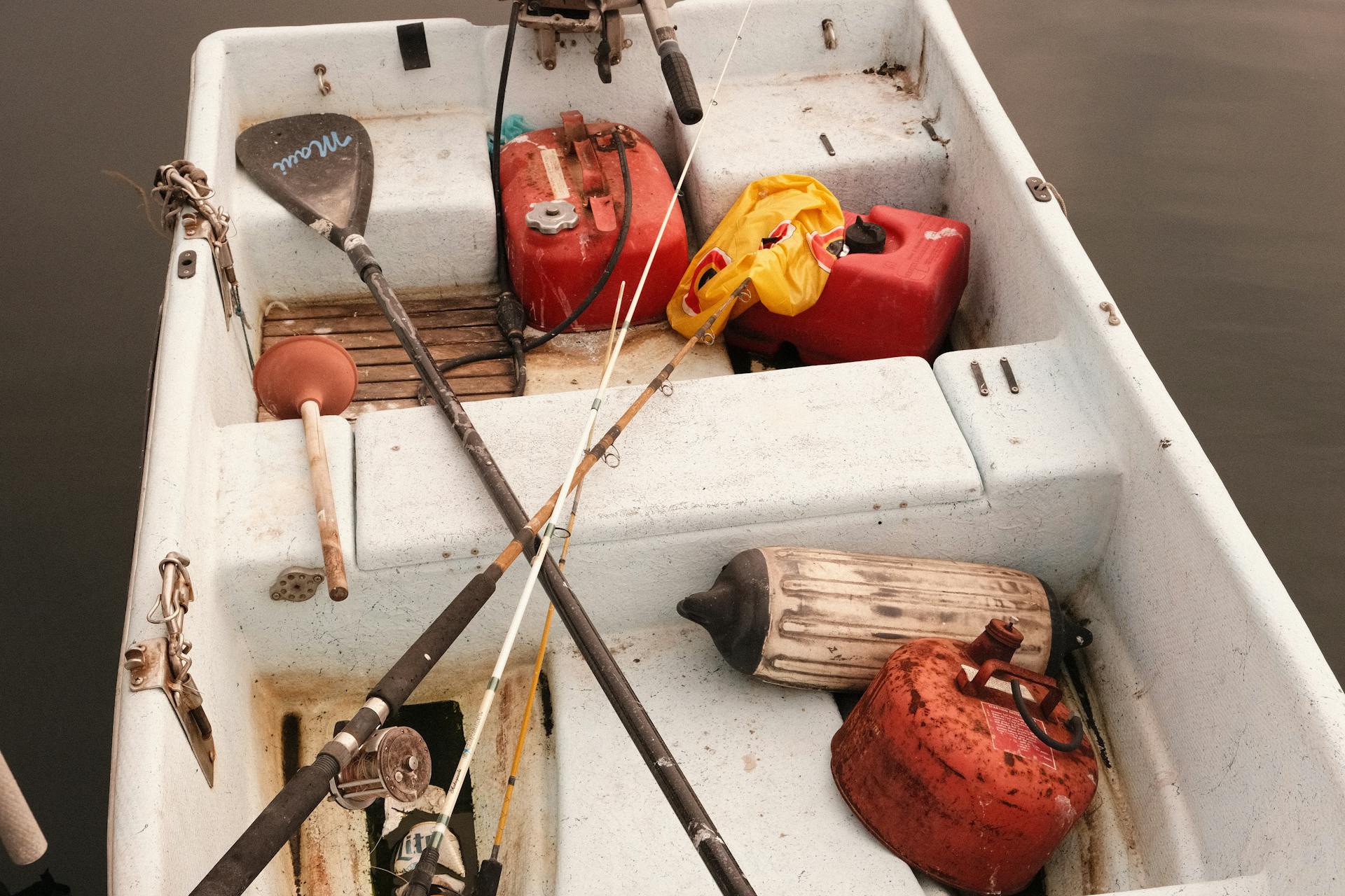 Compact fishing boat equipped with rods, paddles, and fuel tanks on a serene water body.