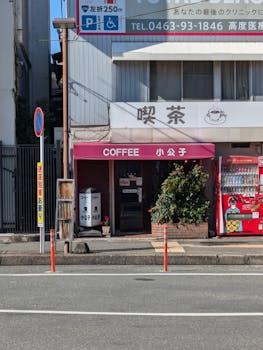 A quaint Japanese coffee shop with vending machines on a sunny city street.