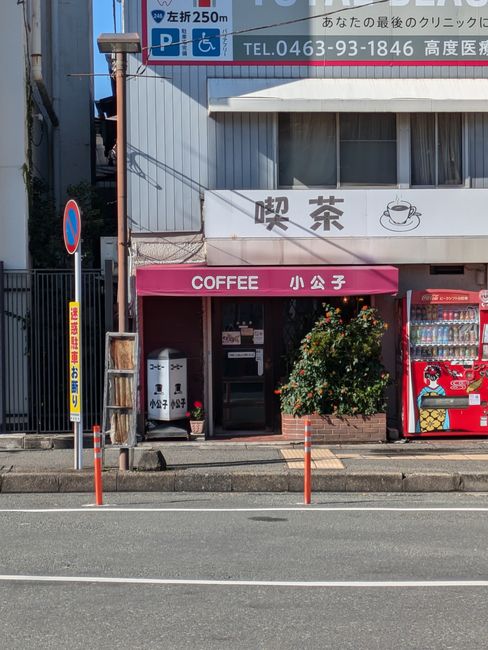 A quaint Japanese coffee shop with vending machines on a sunny city street.