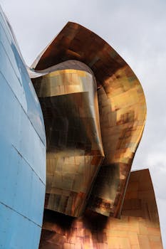 Modern architecture featuring gleaming, curved metallic surfaces under a cloudy sky.