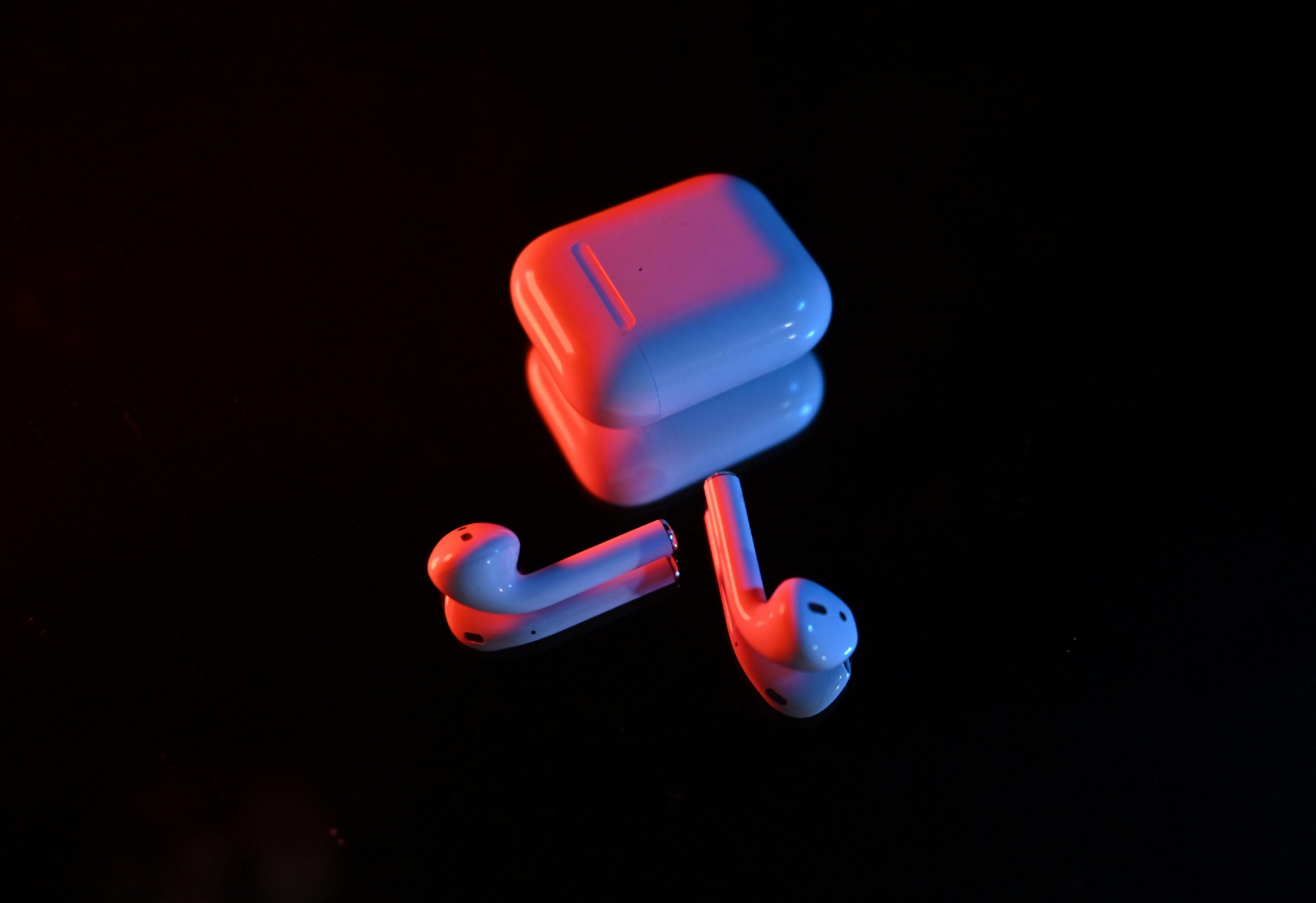 grátis Fones de ouvido sem fio e estojo de carregamento iluminados por luzes vermelhas e azuis em um fundo escuro. Foto profissional