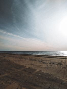 Tranquil sandy beach with calm waves under a vast sky in Leningrad Oblast, Russia.