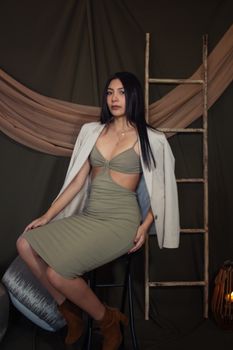 Elegant woman in contemporary attire posing indoors with rustic backdrop.