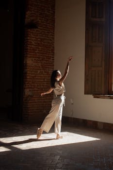 Dancer gracefully poses in a sunlit room with exposed brick walls, capturing movement and artistic expression.