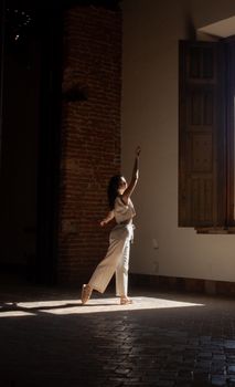 A dancer gracefully posing in a sunlit room with rustic brick walls.