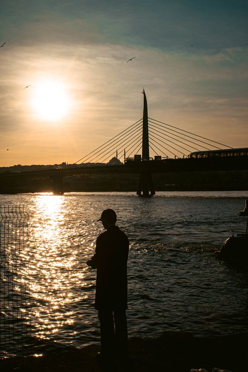 Free A silhouette of a man stands by Istanbul's Golden Horn Bridge during a picturesque sunset. Stock Photo