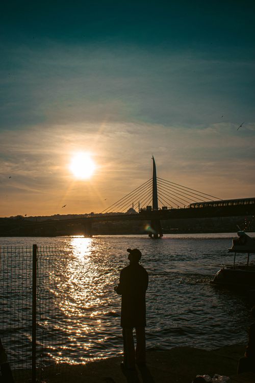 Free A silhouette stands by the shimmering waters of the Golden Horn at sunset in Istanbul. Stock Photo