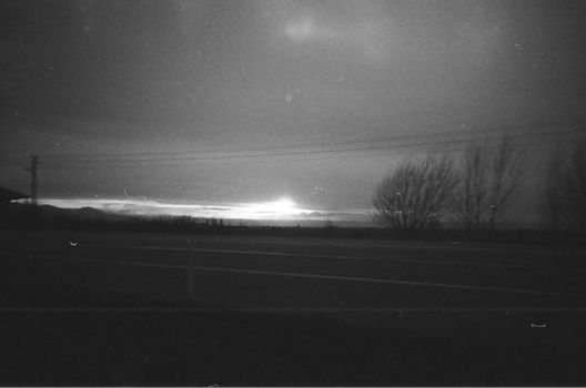 Dramatic black and white sunset view with silhouetted trees and open road.