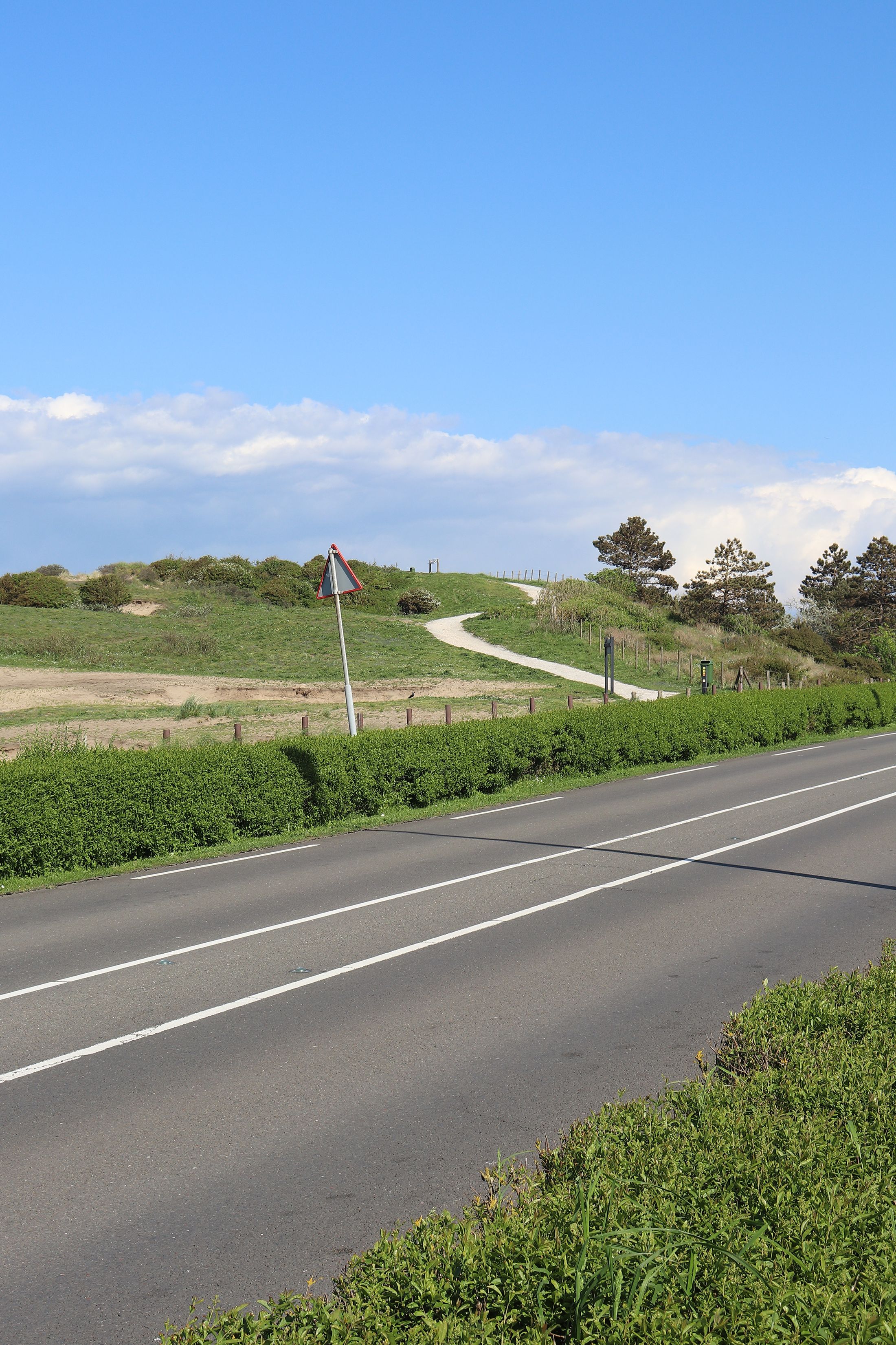 A winding rural road cutting through lush green hills under a blue sky