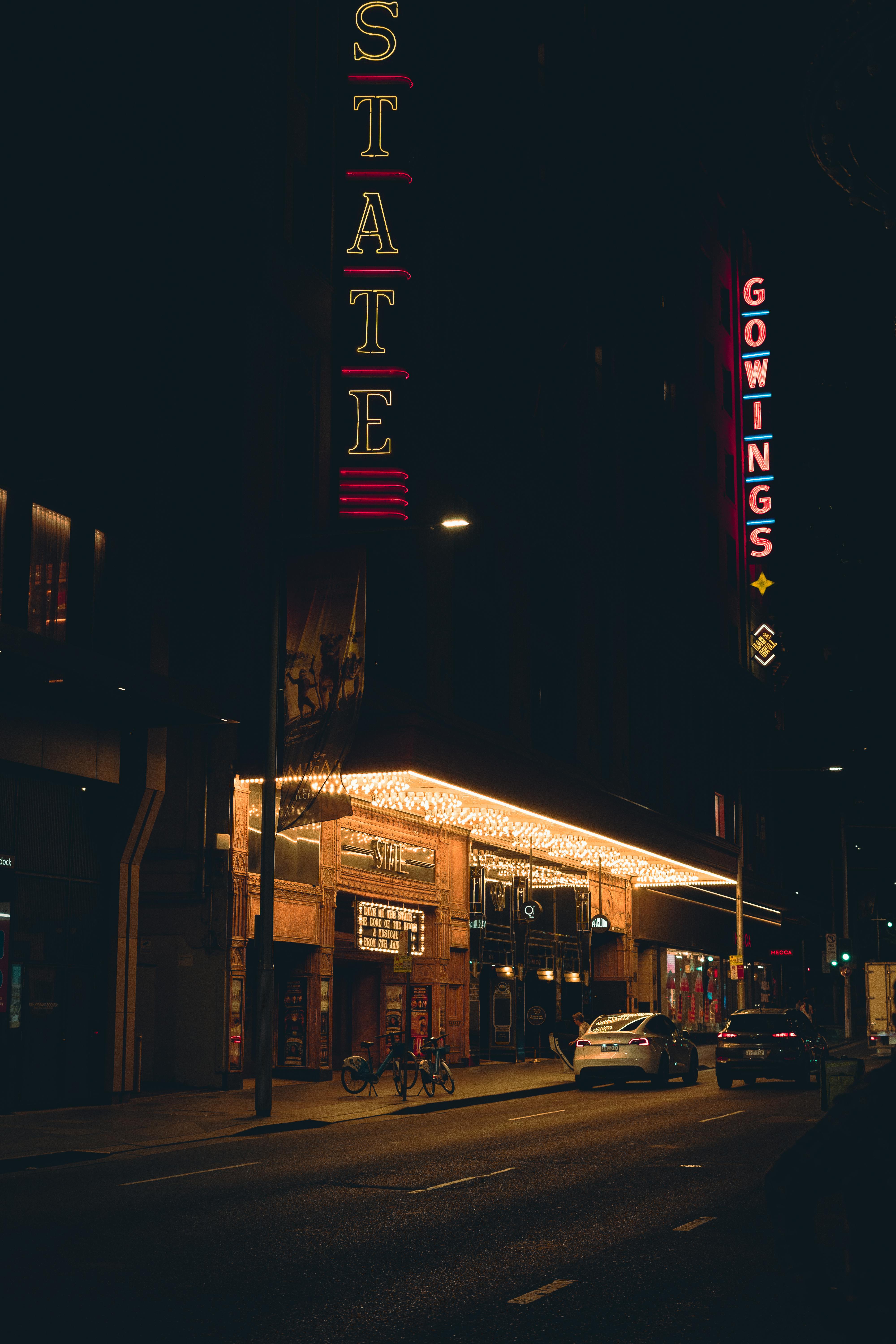 Kostenlos Eine nächtliche Stadtszene mit einem Theater mit Neonlichtern und geparkten Autos entlang der Straße in Sydney. Stock-Foto