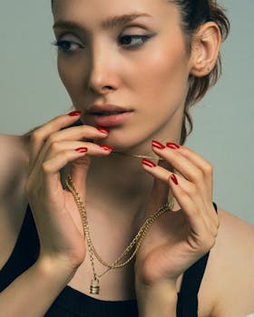 Close-up of a woman with red nails holding a gold necklace, showing elegance and style.
