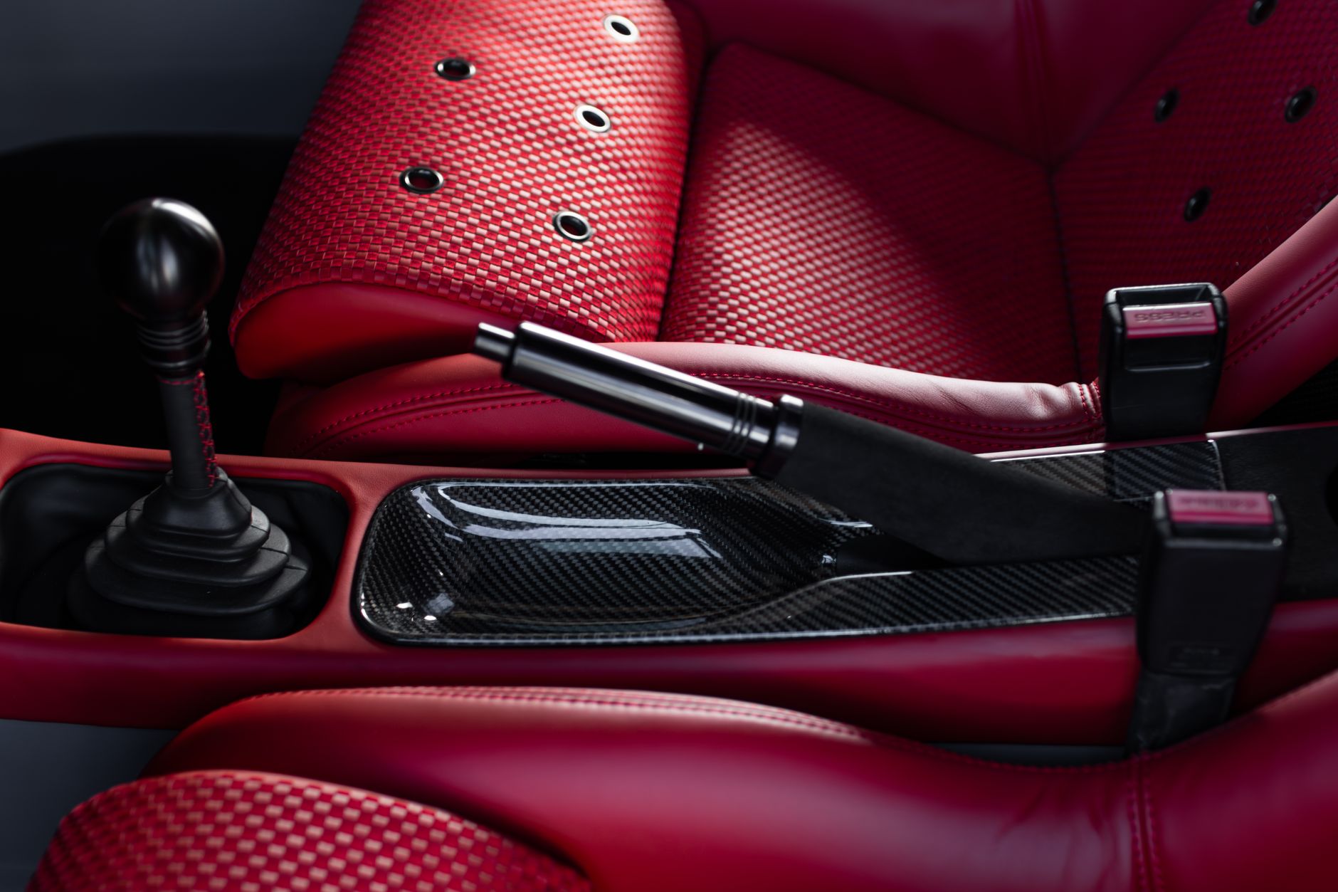 Close-up of a sports car gearshift and red leather seats with carbon fiber detail.