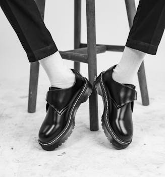 Monochrome image of shiny black leather shoes with white socks on a wooden stool.
