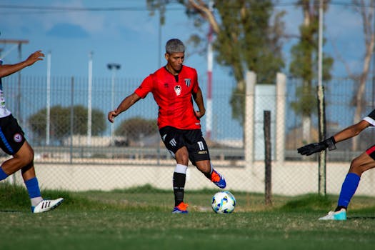 Action shot of a football player in red jersey dribbling during an outdoor match.
