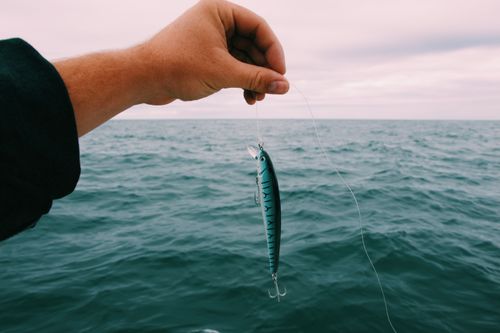Free A hand holding a fishing lure above ocean waters, ideal for fishing enthusiasts. Stock Photo