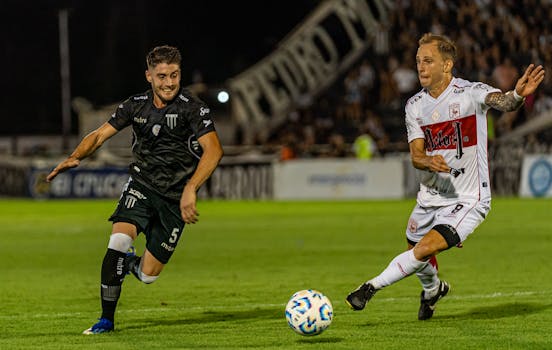 Two male soccer players in action during a night match on a well-lit grassy field.