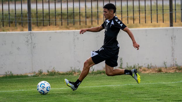 Soccer player in black uniform in motion on a green field outdoors.