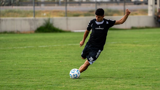 Soccer player in action kicking the ball on a lush green field outdoors.