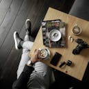 木桌上摆放着杂志、相机和配件，自上而下地展示了一个含咖啡因的停顿