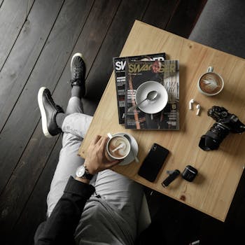 木桌上摆放着杂志、相机和配件，自上而下地展示了一个含咖啡因的停顿