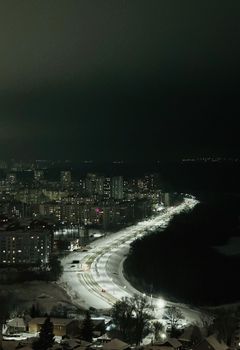 Aerial view of a city at night with snow-covered roads lined by illuminated buildings.