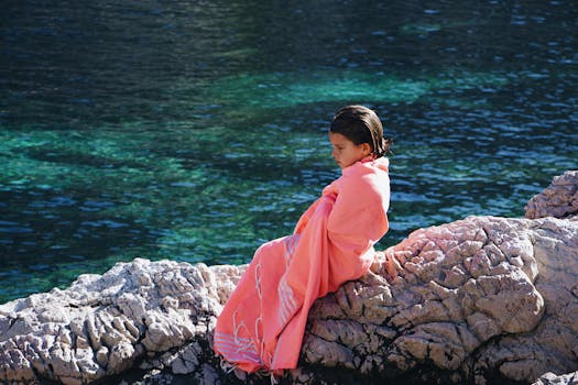 一个裹着毛巾的年轻女孩坐在宁静的湖边沉思，享受着户外活动